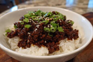 A white bowl filled with white rice topped with saucy Instant Pot Korean Beef, garnished with green onions and sesame seeds.