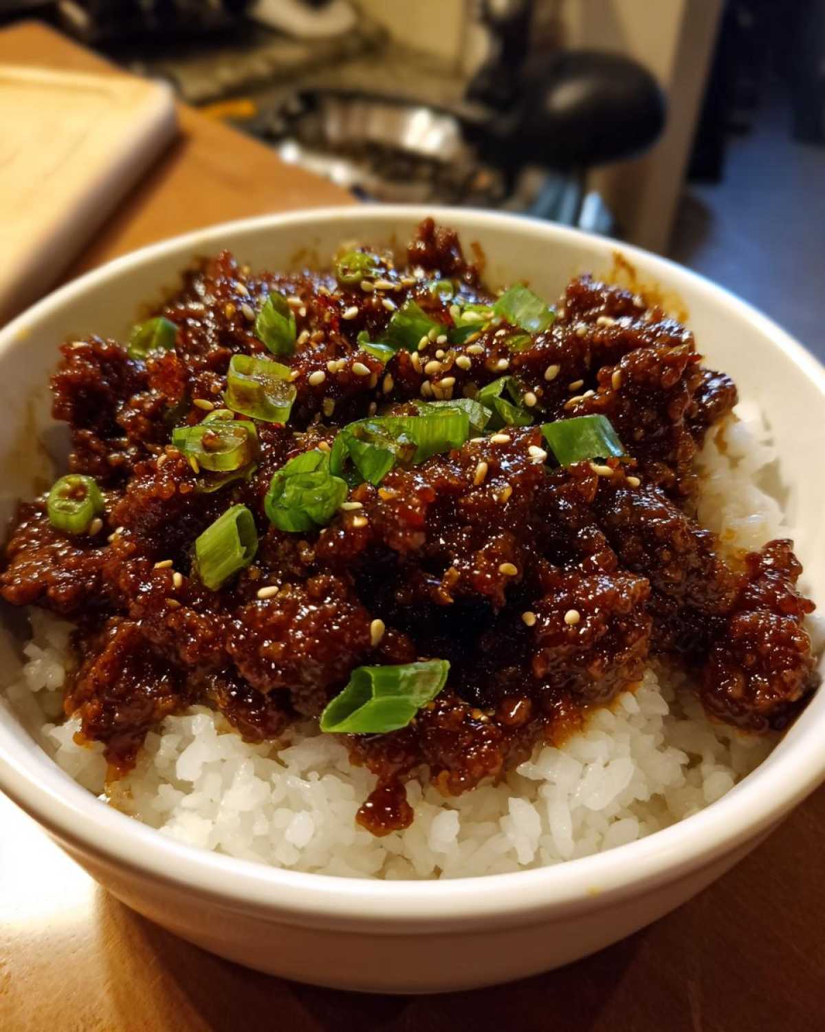 Close-up of a white bowl filled with white rice topped generously with saucy Instant Pot Korean Beef and garnished with green onions and sesame seeds.