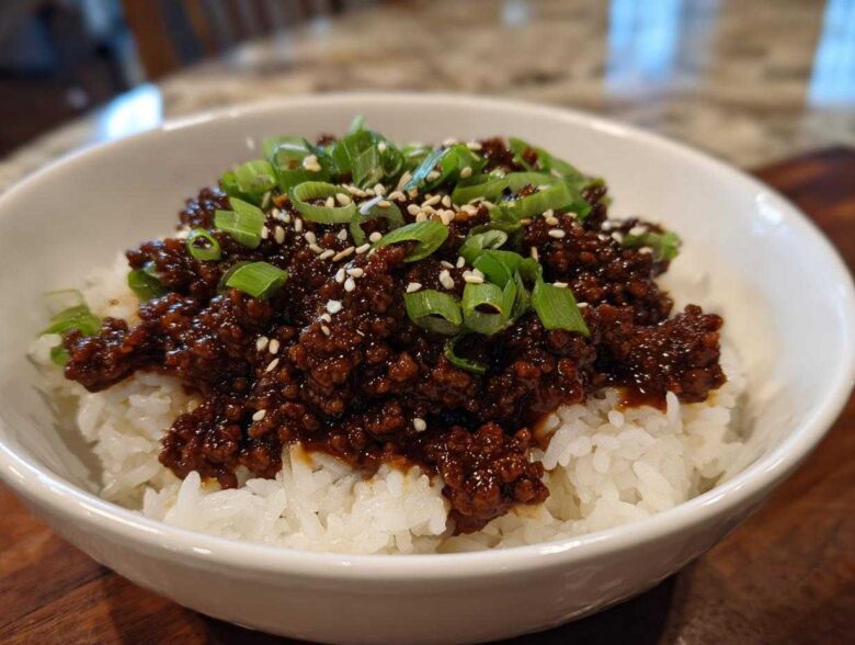 A white bowl filled with white rice topped with saucy Instant Pot Korean Beef, garnished with green onions and sesame seeds.