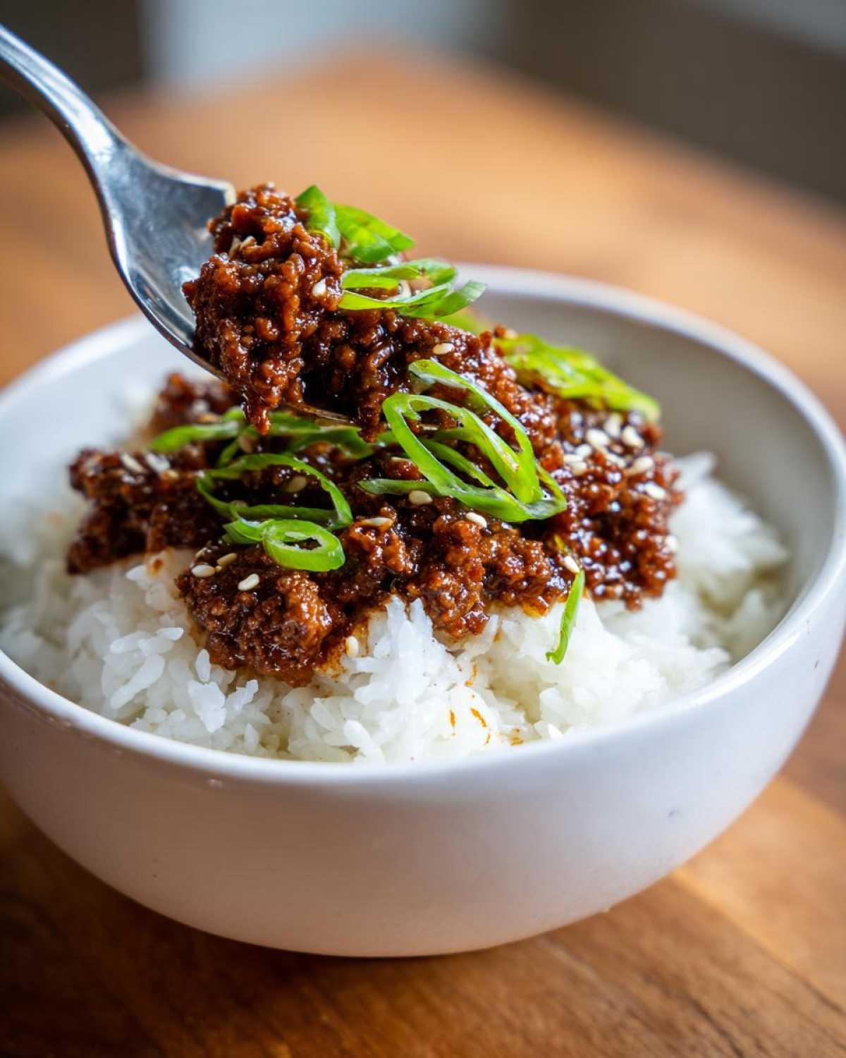 A fork lifting a spoonful of saucy Instant Pot Korean Beef over a bed of white rice, garnished with green onions.