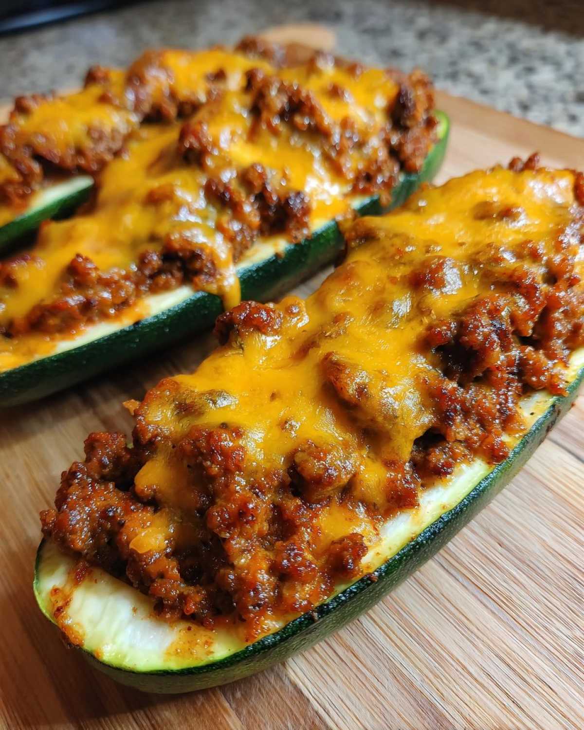 Two Keto Cheesy Taco Stuffed Zucchini Boats filled with seasoned ground meat and melted cheddar cheese.