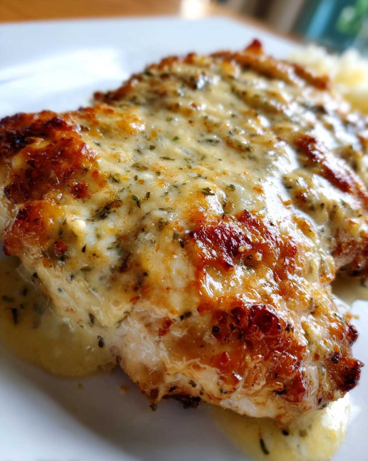 Close-up of a golden-brown piece of chicken topped with melted, creamy garlic parmesan sauce in a Keto Creamy Garlic Parmesan Chicken Bake.