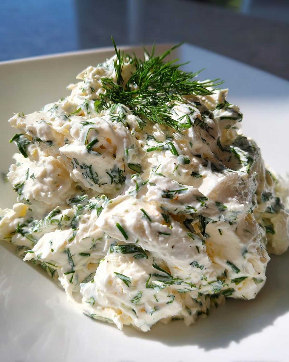 A mound of Keto Creamy Herb Deviled Egg Salad mixed with fresh green herbs and topped with a sprig of dill.