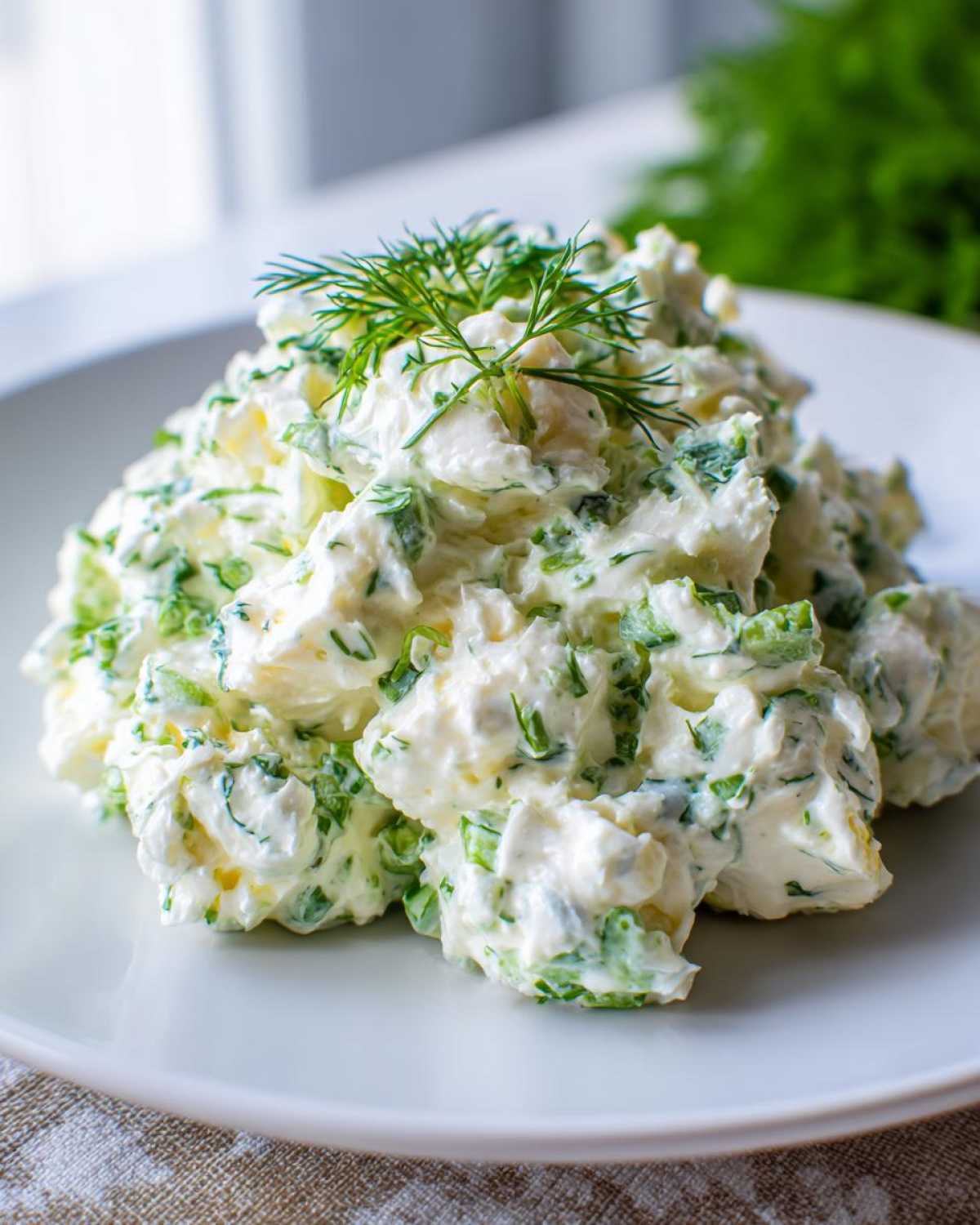 A mound of Keto Creamy Herb Deviled Egg Salad mixed with green herbs, topped with fresh dill, served on a white plate.