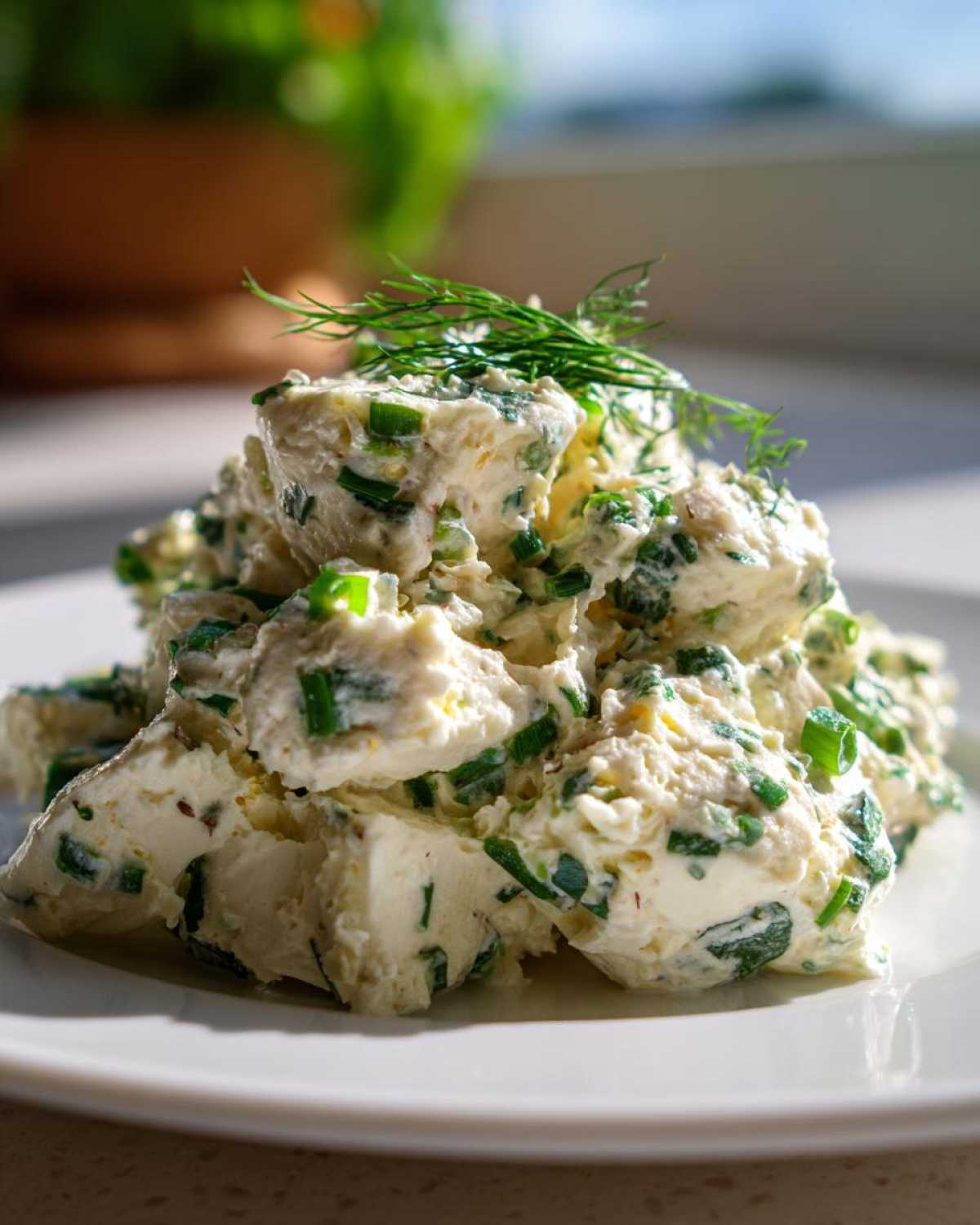 A mound of Keto Creamy Herb Deviled Egg Salad mixed with chopped green herbs, garnished with dill, on a white plate.
