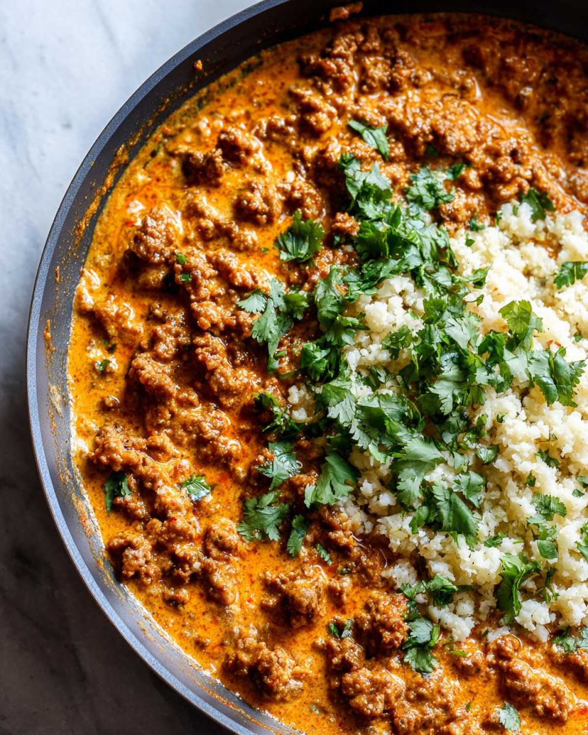 Overhead view of Keto Creamy Taco Skillet with ground meat in a rich sauce next to cauliflower rice and topped with cilantro.