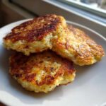 Three golden-brown, crispy Keto Crispy Cauliflower Hash Browns stacked slightly on a white plate.