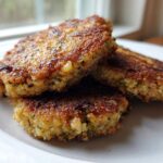 Three golden brown, pan-fried Keto Crispy Cauliflower Hash Browns stacked on a white plate.