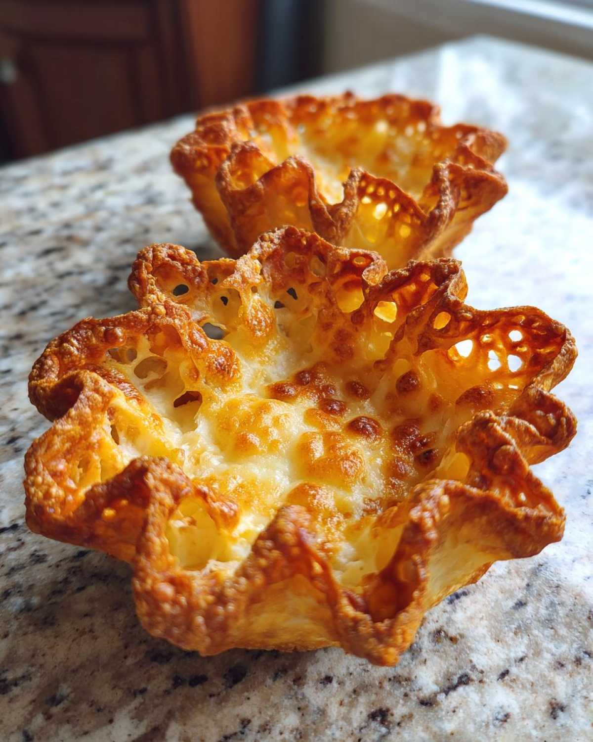 Two golden brown, crispy Keto Crispy Cheese Taco Shell Bowls resting on a granite countertop.