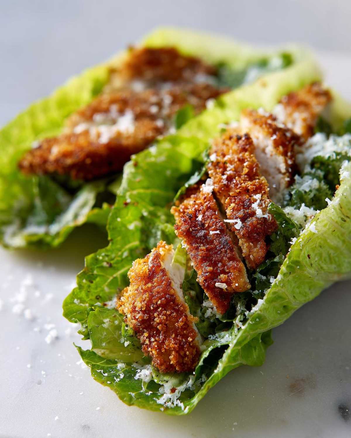 Close-up of Keto Crispy Chicken Caesar Salad Wraps featuring breaded chicken strips in romaine lettuce cups with Caesar dressing and parmesan.