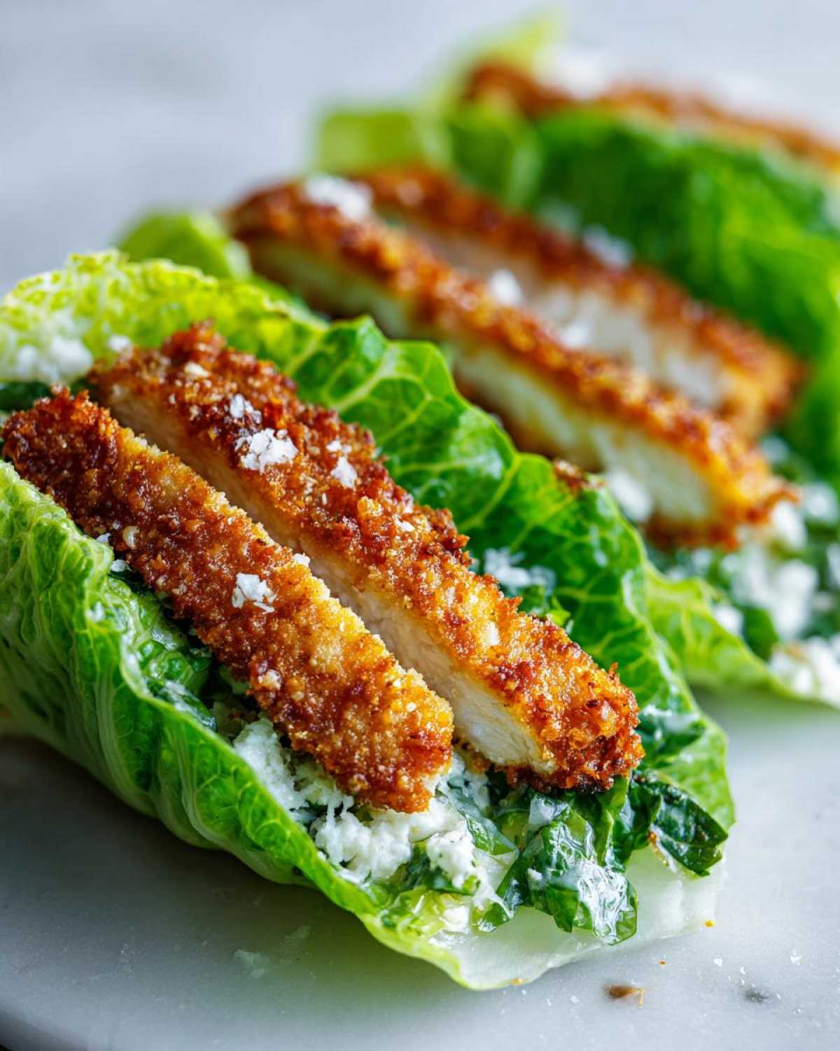 Close-up of Keto Crispy Chicken Caesar Salad Wraps featuring golden fried chicken strips on romaine lettuce with creamy dressing.