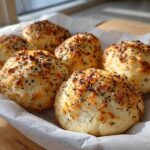 Six golden-brown Keto Everything Bagel Cloud Bread rolls topped with black seeds, resting in parchment paper.