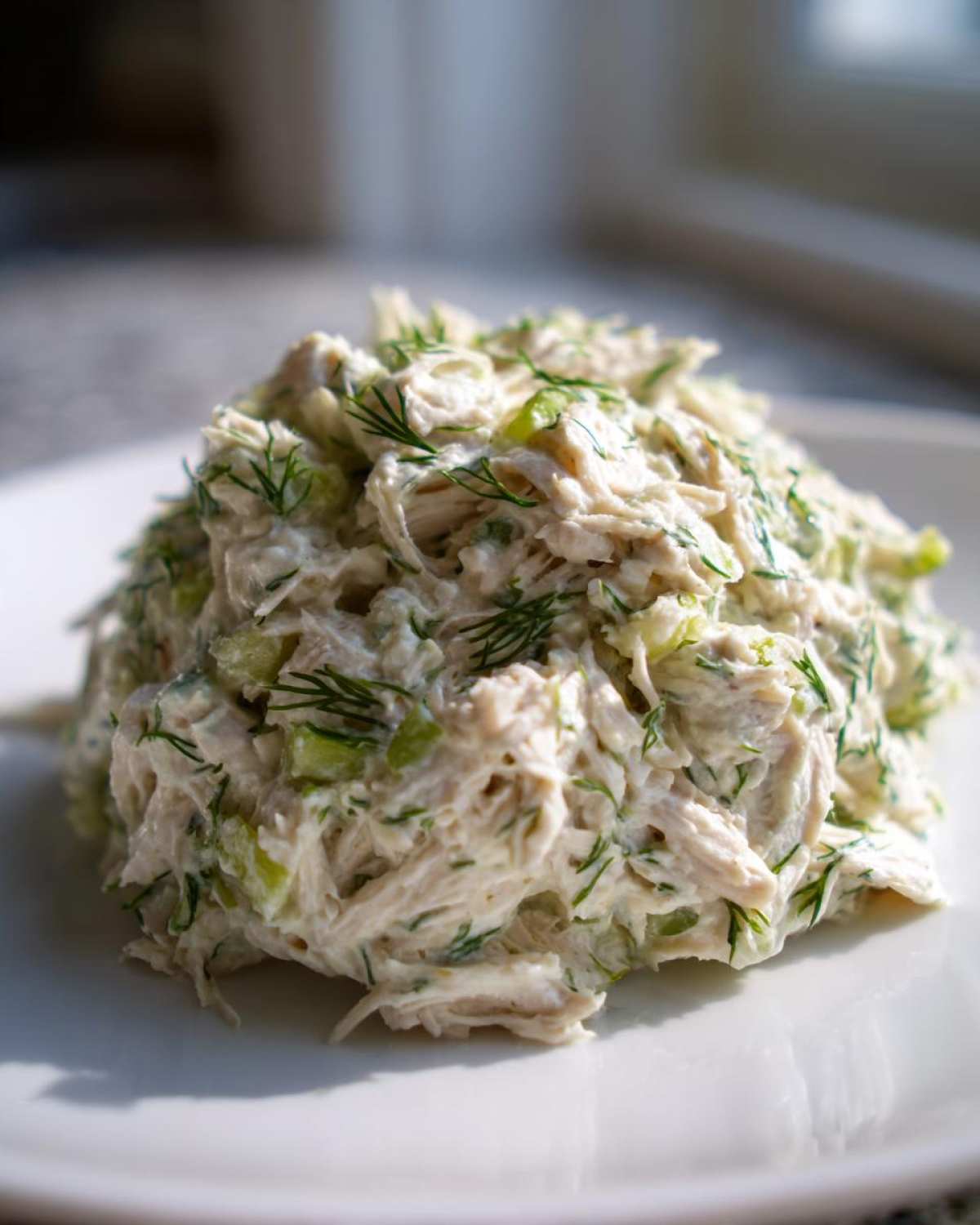 A mound of creamy Keto Lemon Herb Chicken Salad mixed with celery and fresh dill, served on a white plate.