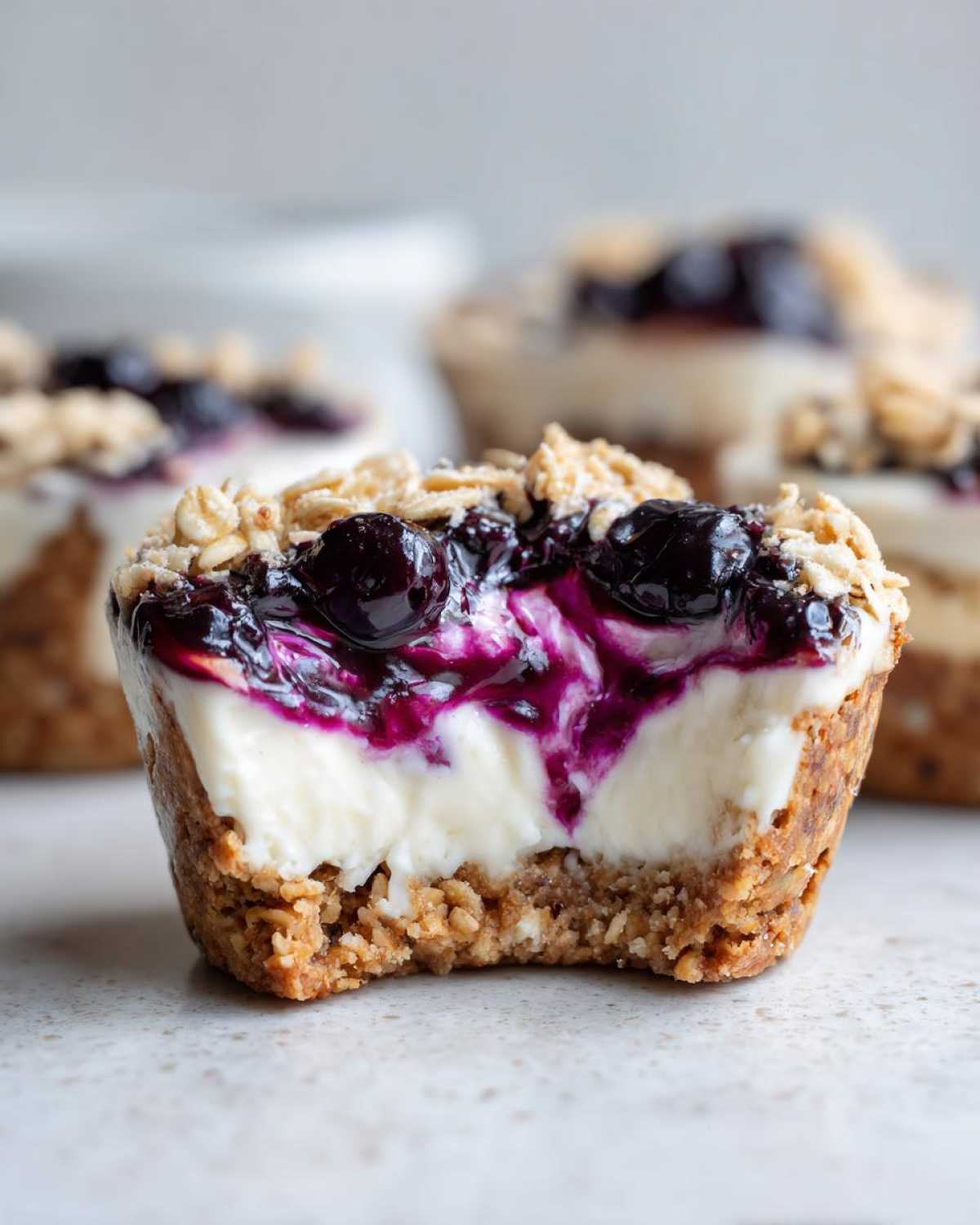 Close-up of a No-Bake Blueberry Cheesecake Oat Cup with a bite taken out, showing creamy filling and blueberry topping.