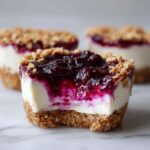 A close-up view of a No-Bake Blueberry Cheesecake Oat Cup with a bite taken out, showing the creamy filling and blueberry topping.
