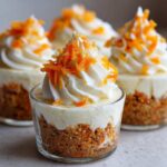 Close-up of a No-Bake Carrot Cake Cheesecake Cup topped with piped cream cheese frosting and shredded carrots.