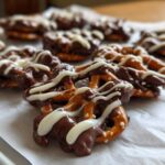 Close-up of several No-Bake Chocolate Covered Pretzel Clusters drizzled with white chocolate on parchment paper.