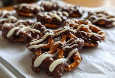Close-up of several No-Bake Chocolate Covered Pretzel Clusters drizzled with white chocolate on parchment paper.