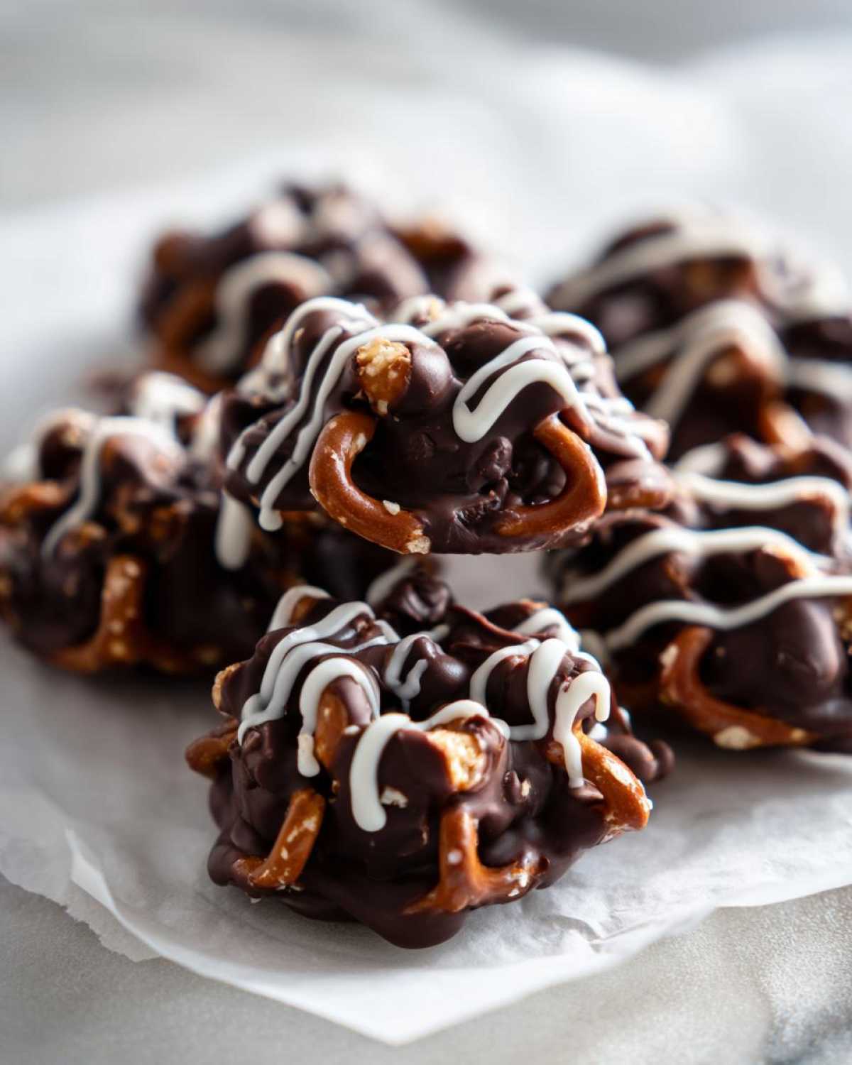 Close-up of several No-Bake Chocolate Covered Pretzel Clusters drizzled with white chocolate on parchment paper.