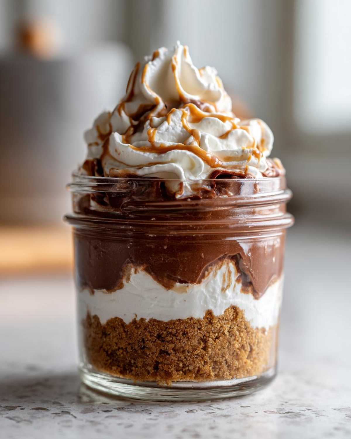 A single serving of No-Bake Chocolate Peanut Butter Pie Jars layered in a glass jar with crust, filling, and whipped cream.
