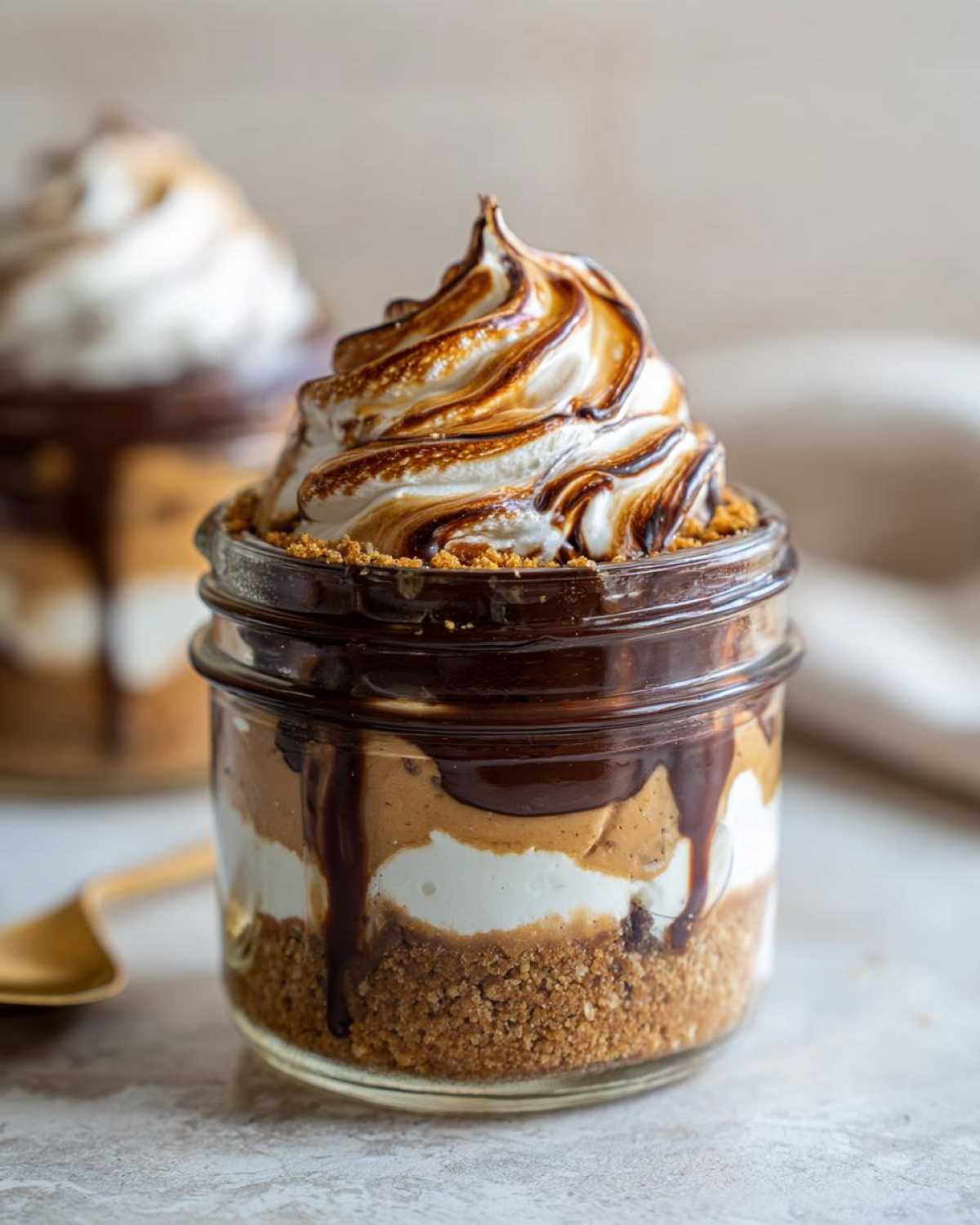 Close-up of a layered No-Bake Chocolate Peanut Butter Pie Jar topped with toasted meringue and chocolate drizzle.
