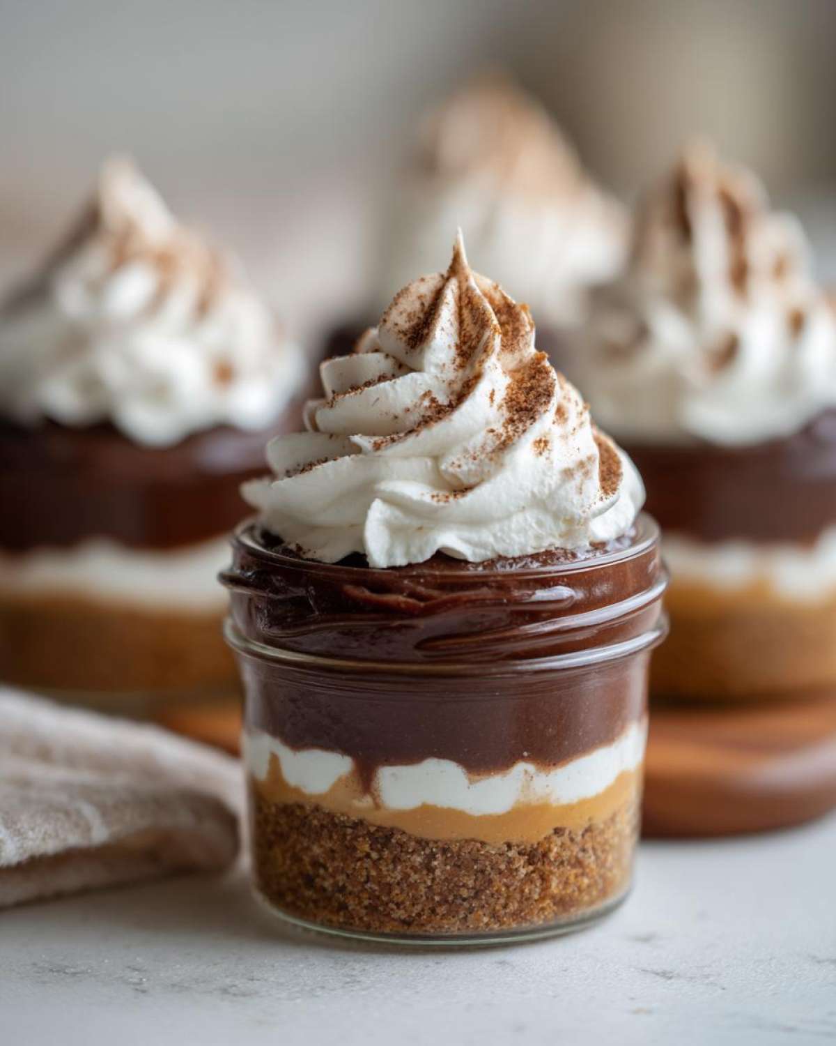 A close-up of a layered No-Bake Chocolate Peanut Butter Pie Jar topped with whipped cream and cocoa.