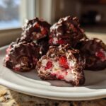 A pile of No-Bake Chocolate Strawberry Yogurt Clusters on a white plate, one is bitten open showing the yogurt and strawberry filling.