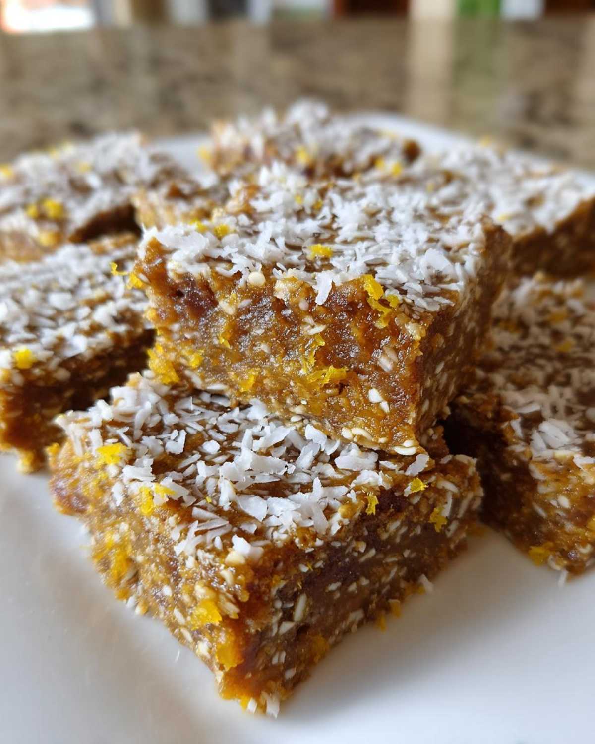 Close-up of stacked No-Bake Lemon Almond Date Bars, featuring a dense texture and topped with shredded coconut and lemon zest.
