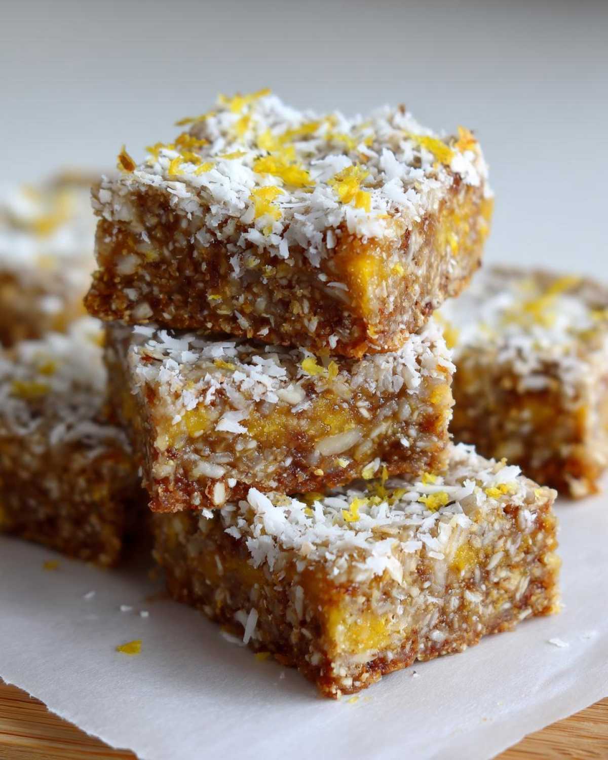 A stack of three No-Bake Lemon Almond Date Bars topped with shredded coconut and bright yellow lemon zest.