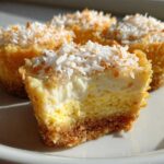 Close-up of a No-Bake Lemon Coconut Cheesecake Cup cut in half, showing graham cracker crust and creamy filling topped with toasted coconut.