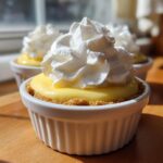 A close-up of a No-Bake Lemon Cream Pie Cup topped with a swirl of whipped cream, sitting on a wooden surface.