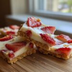 Close-up of stacked No-Bake Lemon Strawberry Cheesecake Bark squares on a wooden board.