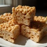 Four squares of gooey No-Bake Peanut Butter Rice Cereal Bars stacked slightly on a white plate.