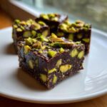 Close-up of rich, dark chocolate fudge squares studded with bright green pistachios, ready to eat.
