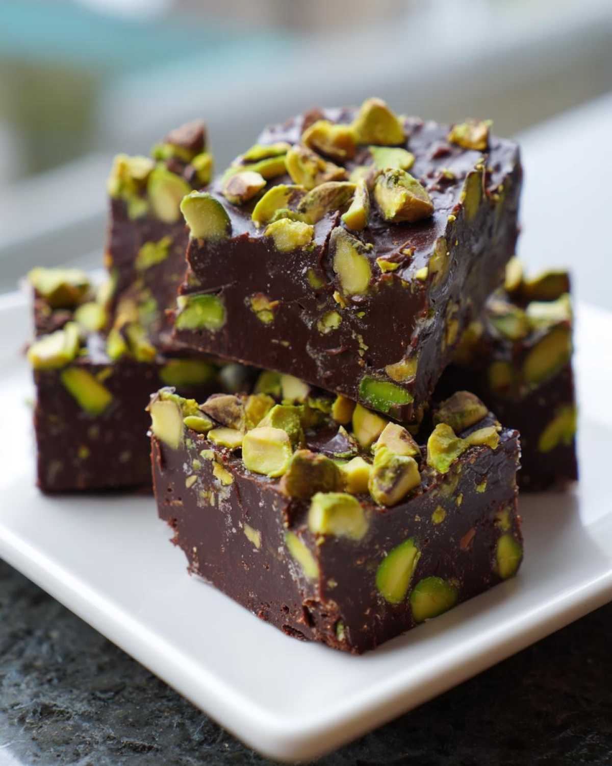 A stack of rich, dark No-Bake Pistachio Chocolate Fudge Squares topped with chopped green pistachios.