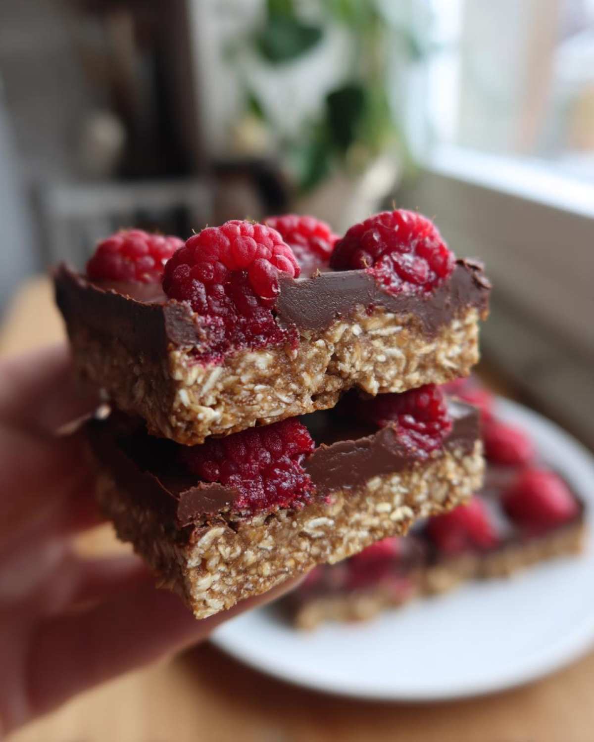 Two stacked bars of No-Bake Raspberry Chocolate Oat Slice, showing the oat base, chocolate layer, and fresh raspberries on top.