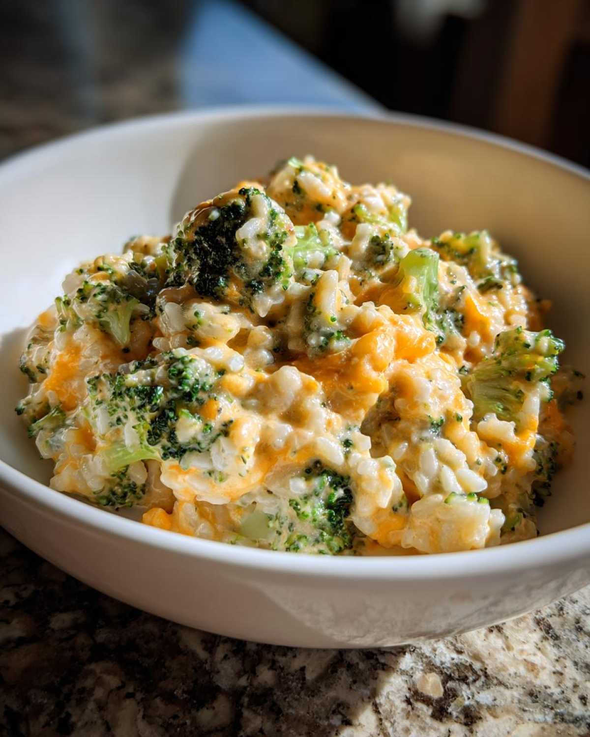A close-up view of a white bowl filled with One-Pot Creamy Broccoli Cheddar Rice, showing melted cheese and bright green broccoli florets.