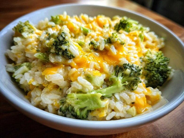Close-up of a white bowl filled with One-Pot Creamy Broccoli Cheddar Rice, featuring melted cheese and bright green broccoli florets.