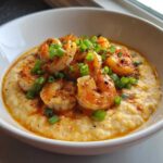 A close-up of One-Pot Creamy Cajun Shrimp and Grits topped with bright green scallions in a white bowl.