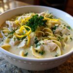 Close-up of a bowl of One-Pot Creamy Lemon Chicken Noodle Soup topped with lemon zest and parsley.