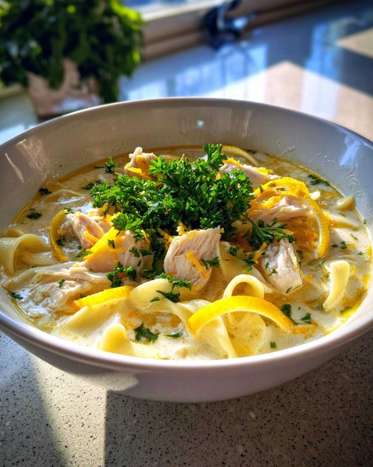 Close-up of a bowl of One-Pot Creamy Lemon Chicken Noodle Soup topped with shredded chicken and fresh parsley.
