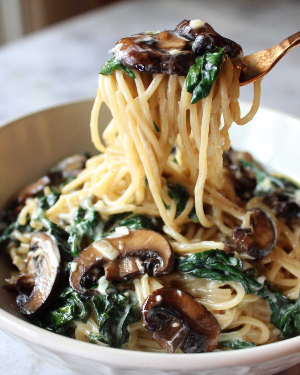 A fork lifting creamy noodles, mushrooms, and spinach from a bowl of One-Pot Creamy Mushroom Spinach Ramen.