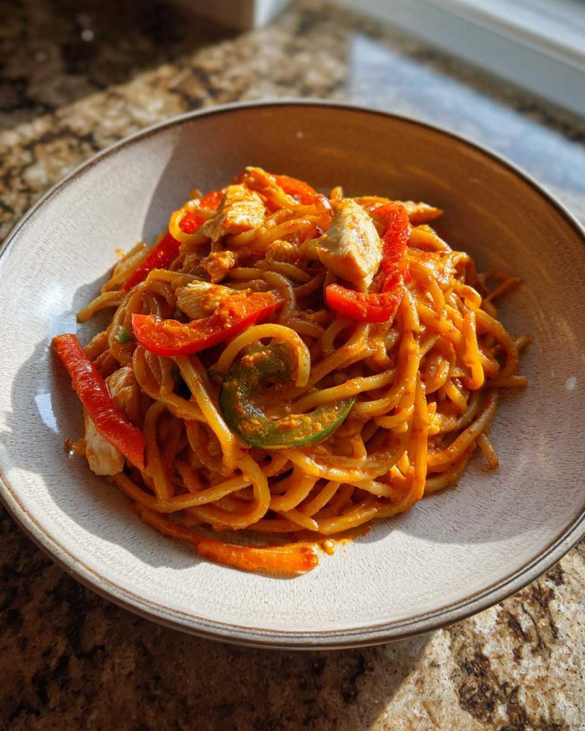A bowl of One-Pot Creamy Thai Red Curry Noodles topped with chicken pieces and sliced red and green bell peppers.
