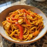A bowl of One-Pot Creamy Thai Red Curry Noodles mixed with chicken pieces and bright red pepper strips.