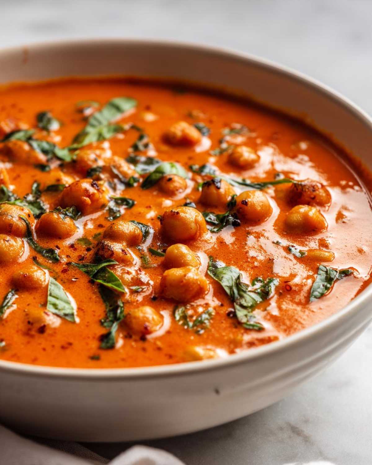 A close-up view of a bowl filled with vibrant One-Pot Creamy Tomato Basil Chickpea Stew, garnished with fresh basil.