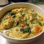 A close-up view of a white bowl filled with One-Pot Creamy Tortellini Minestrone, featuring tortellini, spinach, and carrots in a rich broth.