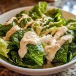 A bowl of crisp green lettuce topped generously with drizzles of Vegan Creamy Lemon Tahini Dressing.