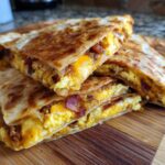 A stack of golden-brown Sheet Pan Breakfast Quesadillas cut into wedges, showing scrambled eggs, cheese, and bacon filling.