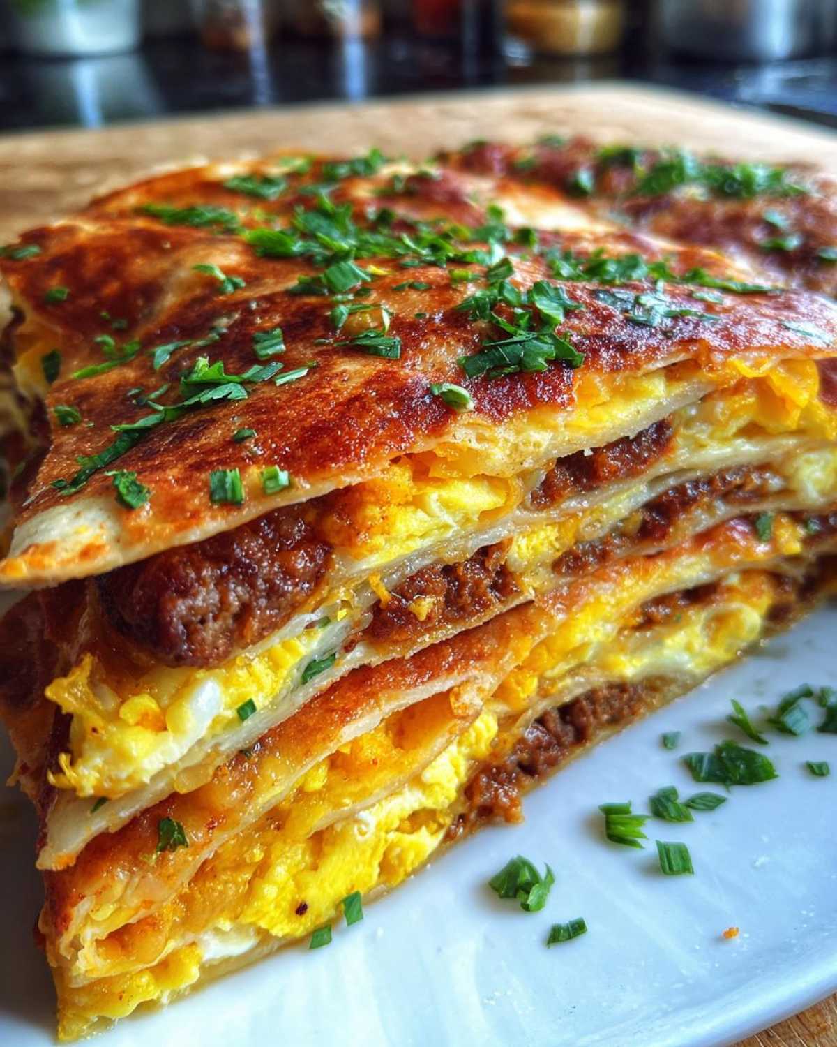 Close-up of stacked, sliced Sheet Pan Breakfast Quesadillas layered with scrambled eggs and sausage, topped with chives.