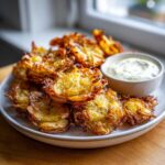 A plate piled high with golden brown Sheet Pan Crispy Smashed Potatoes next to a small bowl of garlic aioli.